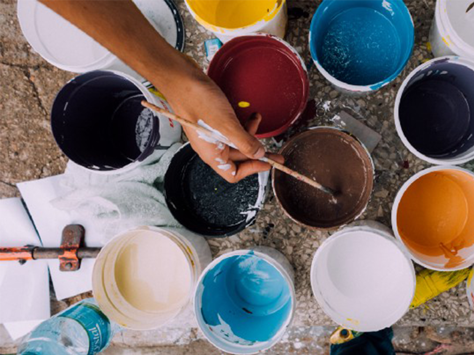 Hand dipping a paint brush into a brown paint container